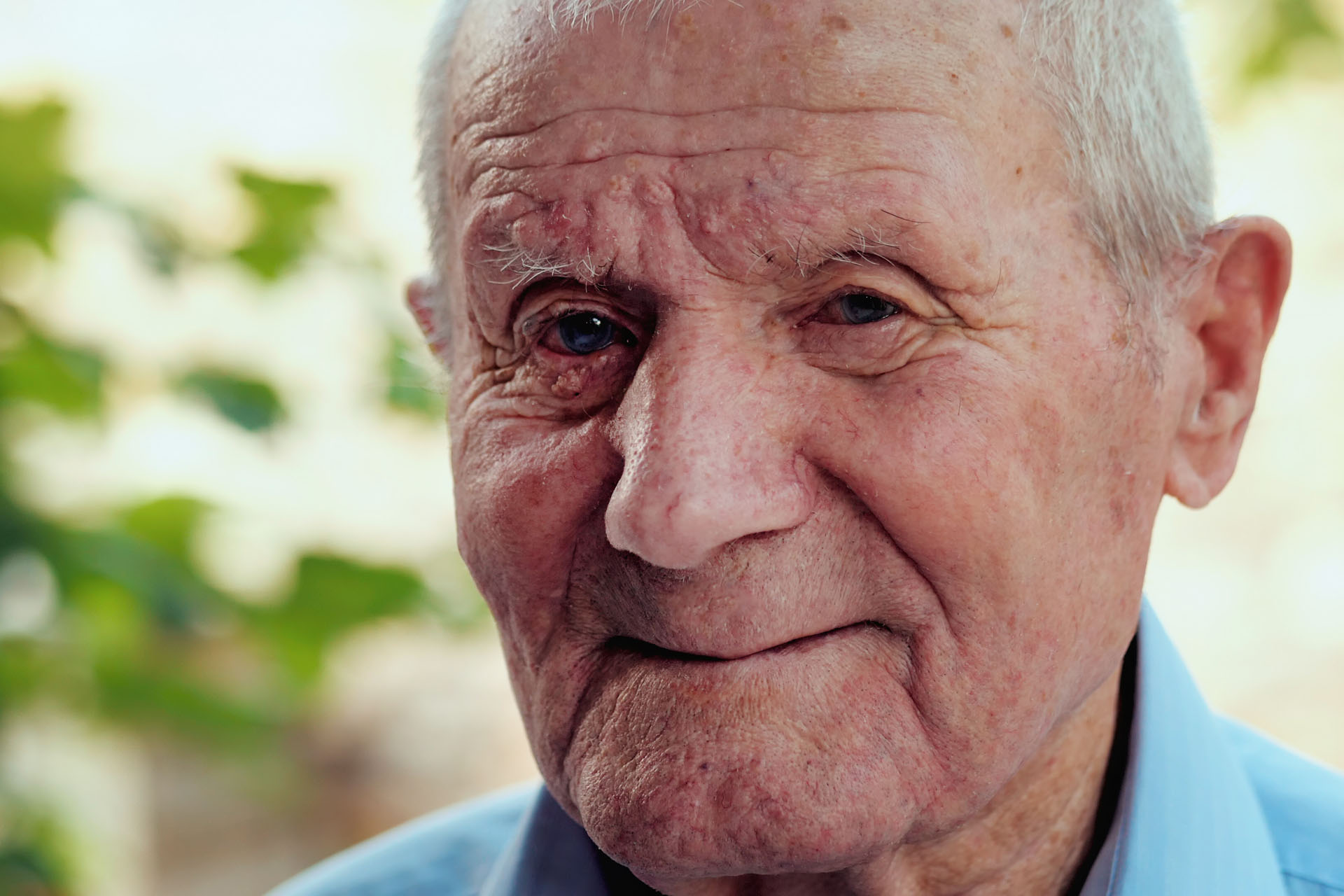 Very old man portrait with emotions. Grandfather is smiling and looking to camera. Portrait: aged, elderly, senior. Close-up of old man sitting alone outdoors.